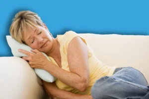 une femme allongée sur son canapé. On la voit triste et dans un mal etre profond.