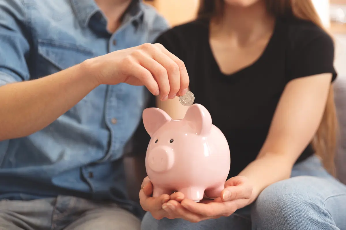 deux personnes tenant une tirelire en forme de cochon et mettant une pièce de monnaie dedans pour illustrer qu'ils font attention à leurs dépenses